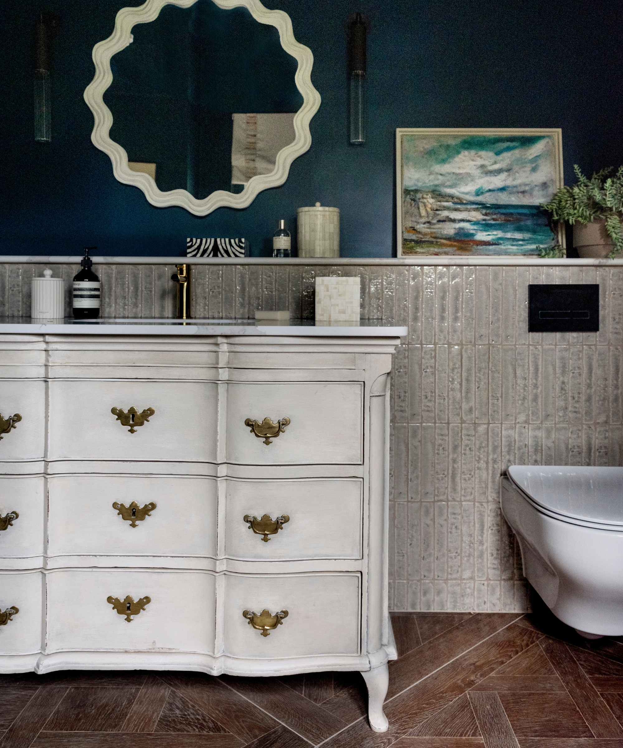 A small bathroom with dark blue walls, gray textured tiles on the lower half of the walls, and a vintage-style vanity designed to look like an antique dresser
