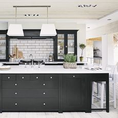 Kitchen with white brick designed tiles on wall wooden flooring with black cabinet white marble countertop and white chairs