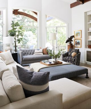Large living room with beamed ceilings, large windows, cream sofa, gray sofa, large square ottoman
