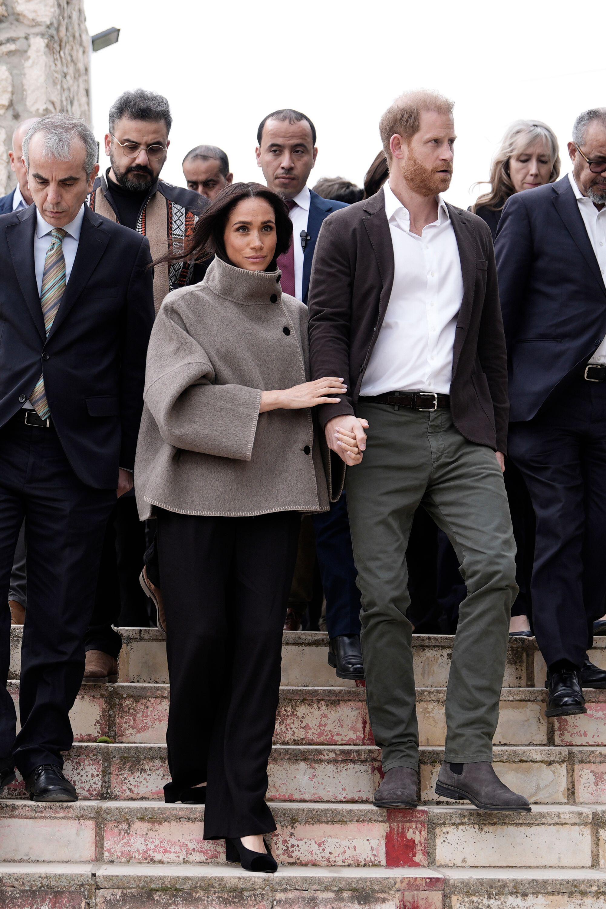 Meghan Markle holding Prince Harry's arm walking down stairs with a group of people