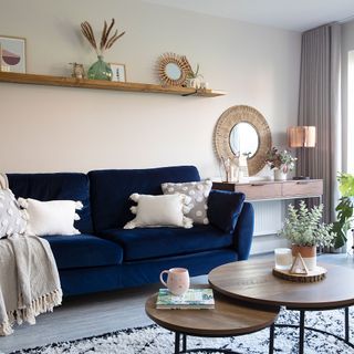 white living room with navy sofa wood flooring wood shelf round nesting coffee tables tassel cushions and throws copper table lamp rattan mirror