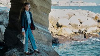 Azzurra Mennella stands on a rocky outcrop next to the ocean in The Lying Life of Adults