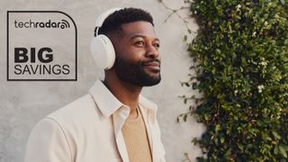 A man wearing a white pair of Sonos Ace headphones, standing in front of a wall. The TechRadar logo and "Big Savings" text are in black, in the top right.