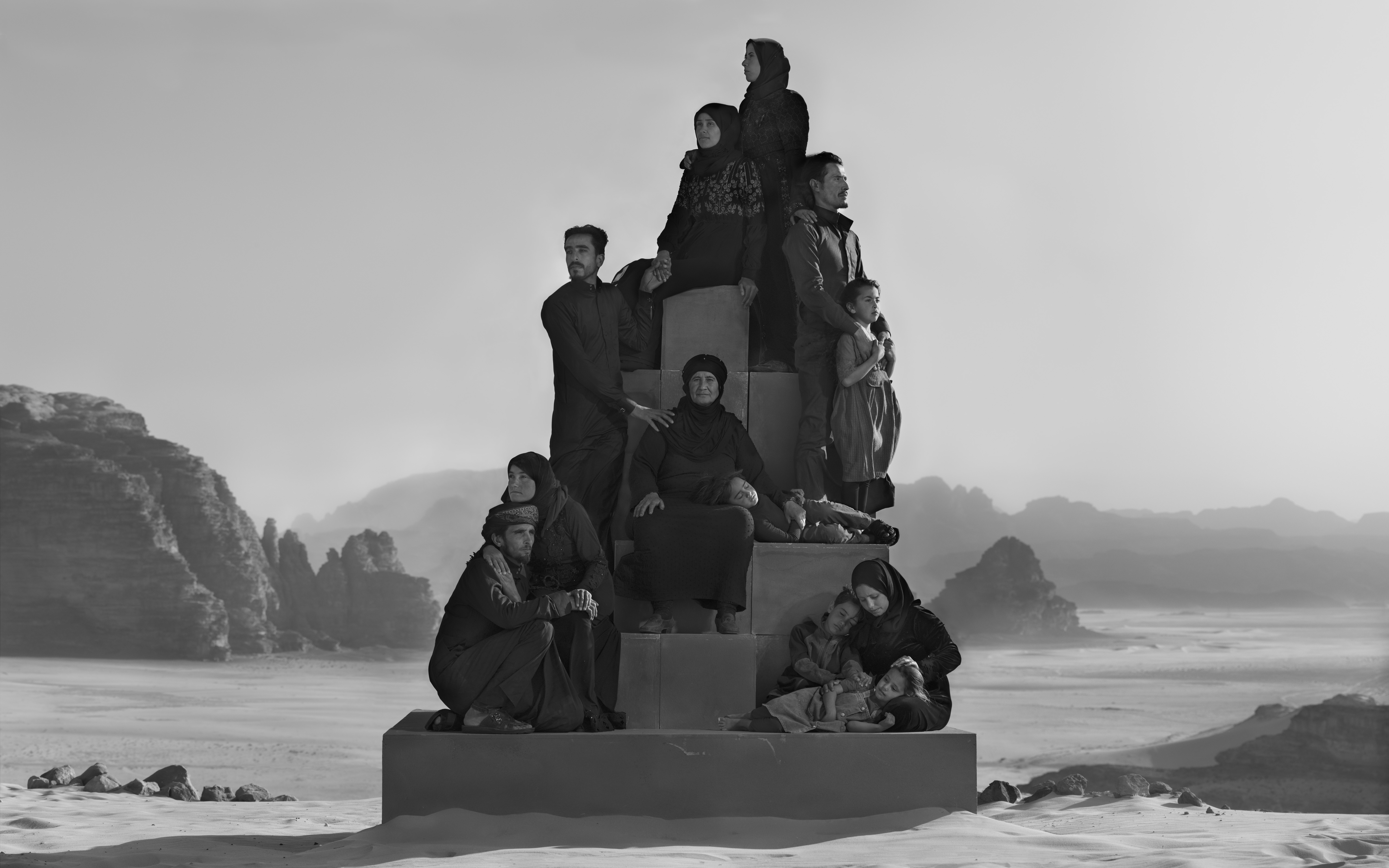 A large family group is posed in a pyramid formation on concrete blocks within a vast, misty desert landscape.