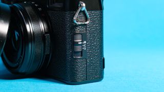 The Fujifilm X100VI mirrorless camera against a blue background with the autofocus control switch showing.