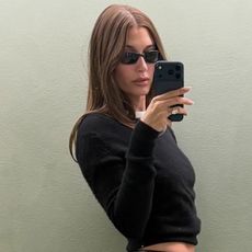 Hailey wears sunglasses, and a black sweater with a white tee.