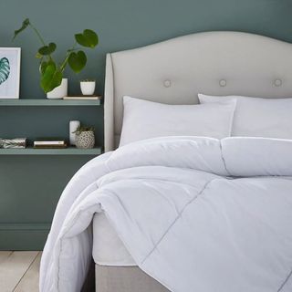A green bedroom with a white duvet and pillows on a pale grey upholstered bed
