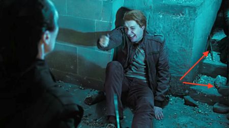 George Weasley sitting on the floor. Red arrows point to a wand a the leg of someone laying near him.