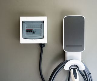 A neatly organized electric vehicle charging station mounted on a wall, featuring a control unit and coiled cable, ideal for home EV charging.