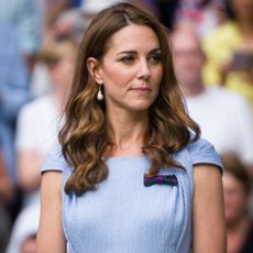 Kate Middleton wears a light blue dress and has long curly brown hair and looks pensive 