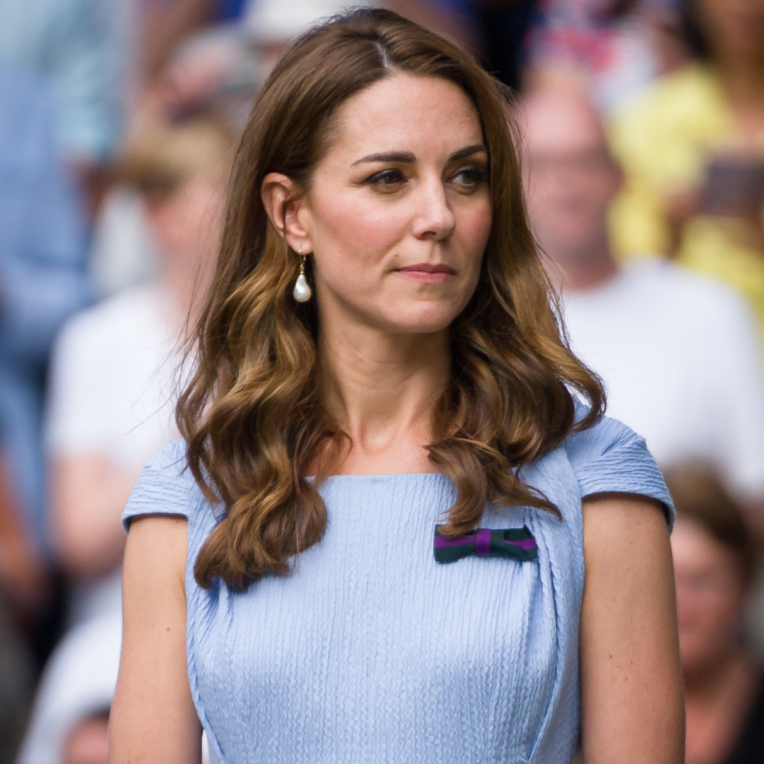 Kate Middleton wears a light blue dress and has long curly brown hair and looks pensive 