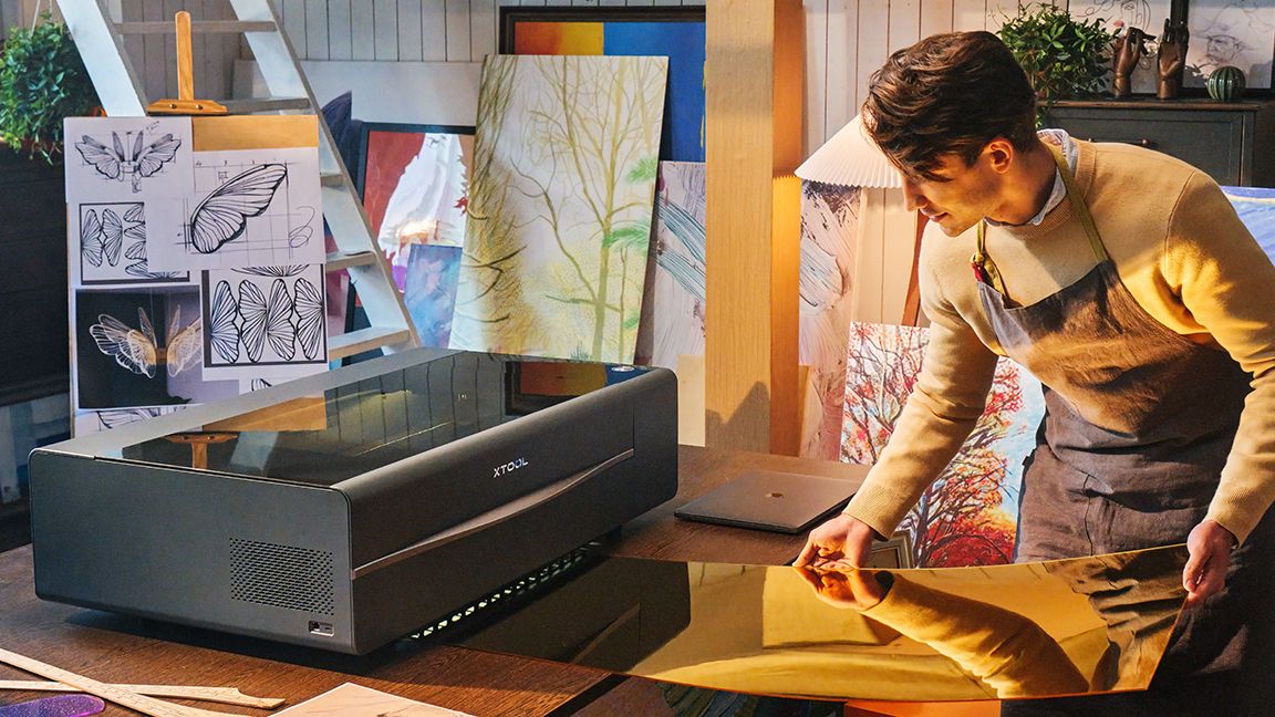 xTool P2 laser cutter; a dark grey laser machine on a table with a man measuring material