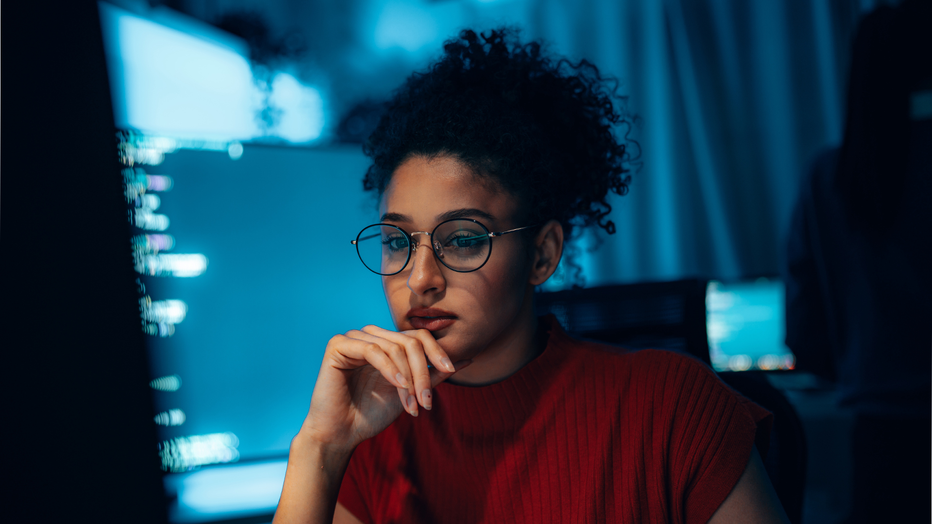 Female developer working in a dimly lit room on a desktop computer while assessing software security debt. 
