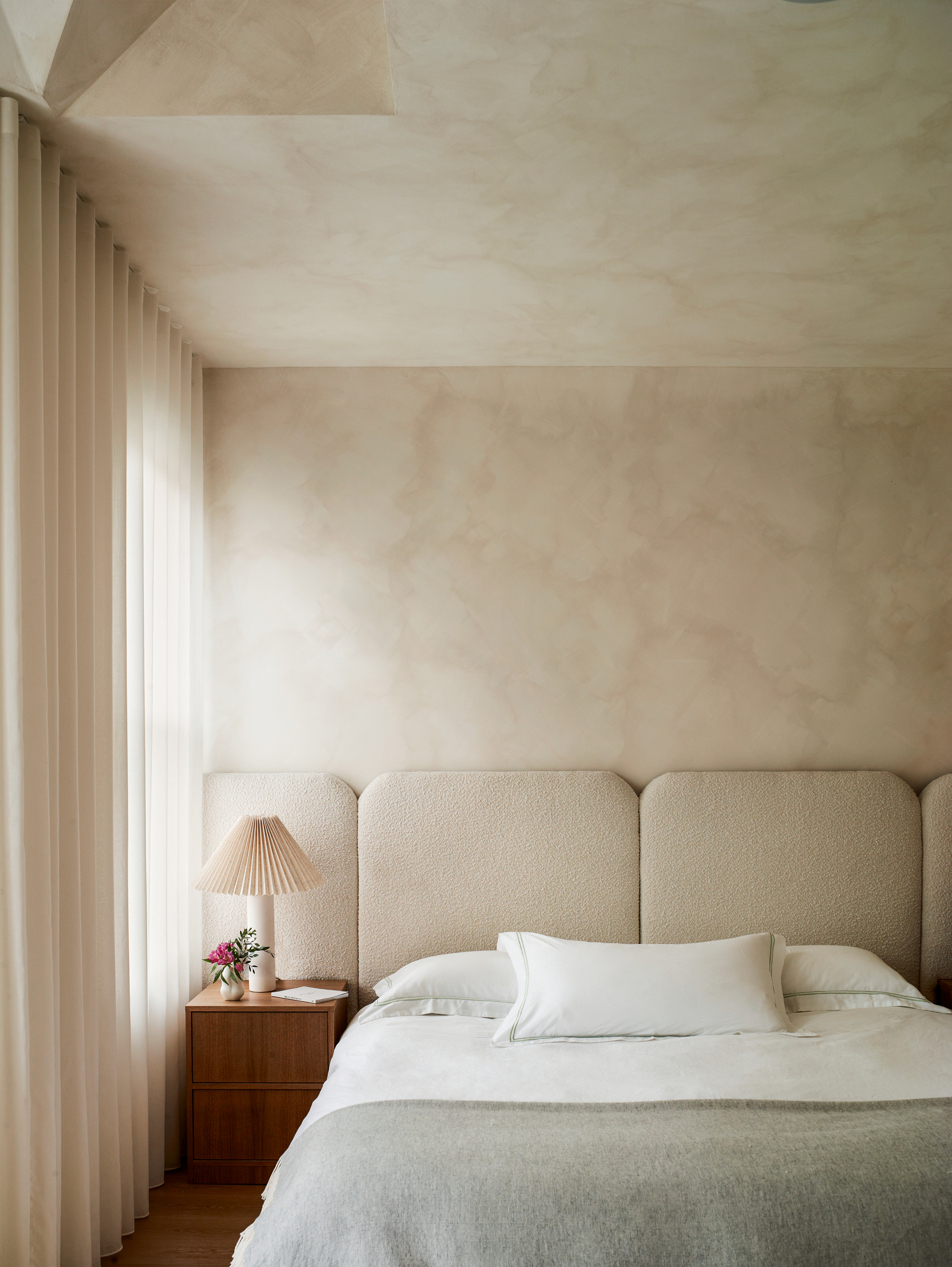 Bedroom with beige limewash walls, beige oversized headboard and grey bed throw