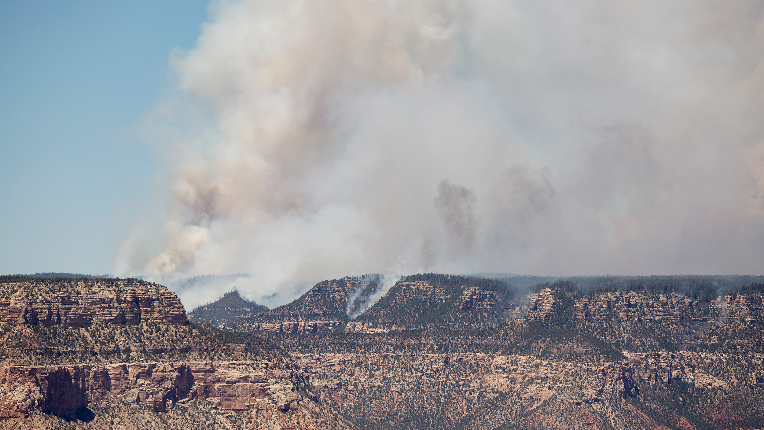 View looking across the Grand Canyon from the south rim towards a section of the Dragon Bravo mega fire burning on the north rim in August 2025 with smoke cloud climbing into the sky