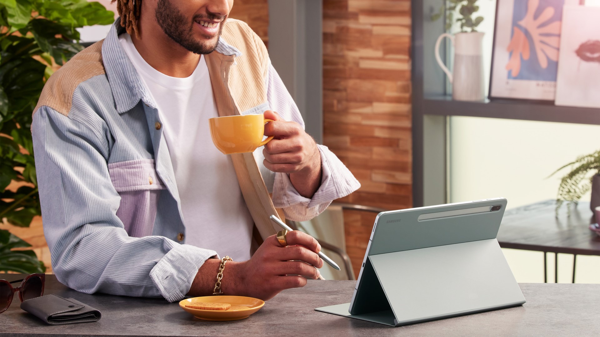 Man drinking from mug, smiling while using Samsung Galaxy Tab S7 FE and S Pen