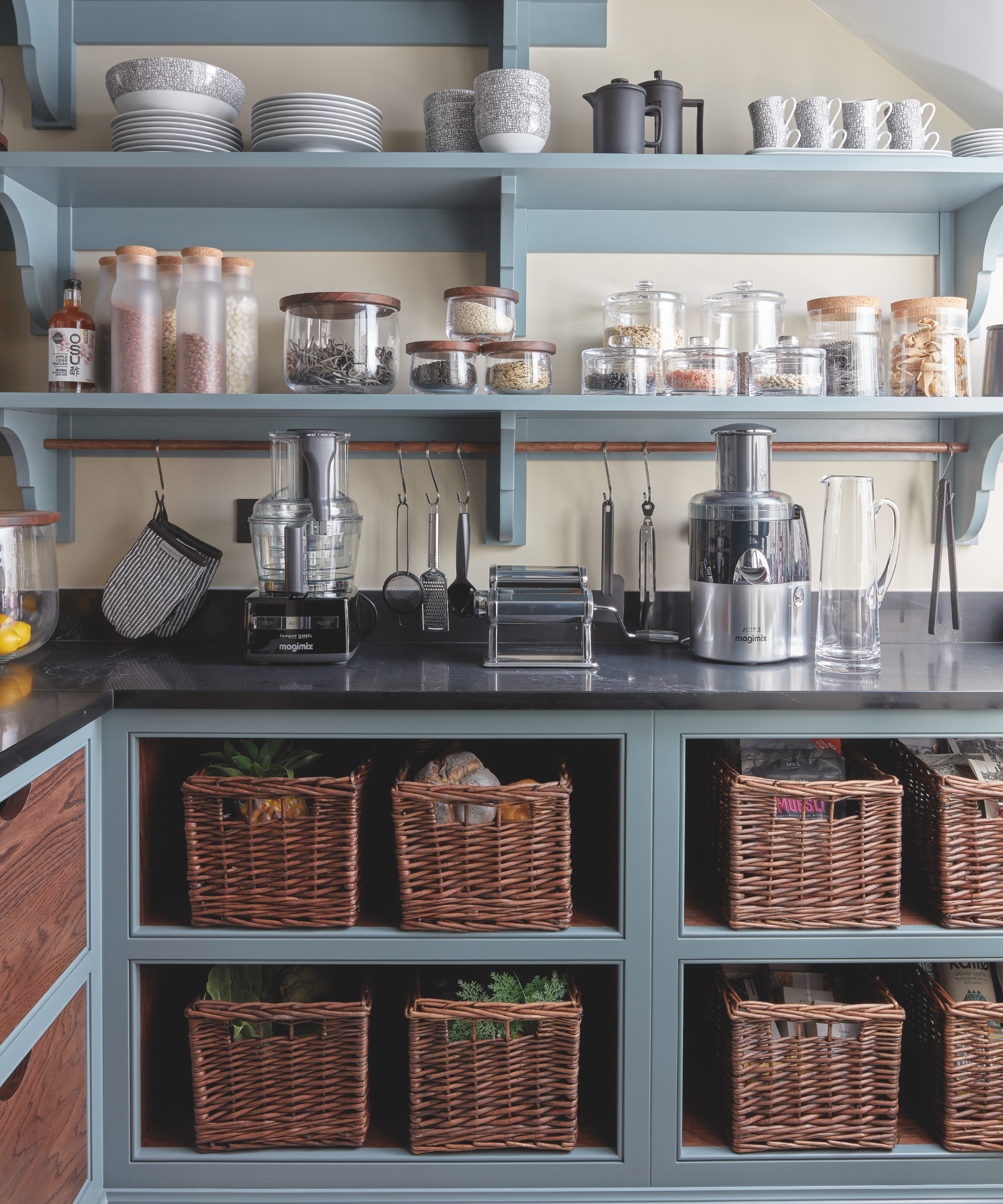 blue kitchen with black countertops, baskets, open shelving, glass jars with food, tableware, brass hanging rail,