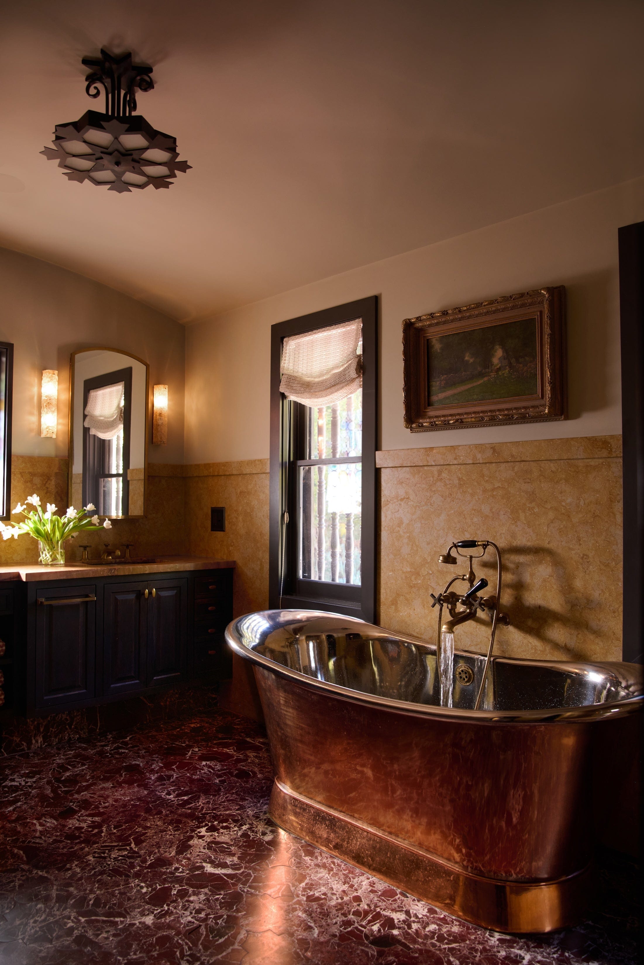 bathroom with red marble flooring, brass bathtub, yellow marble walls and teal cabinets underneath a mirror