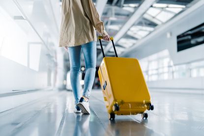 A woman wheels a yellow suitcase through an airport terminal