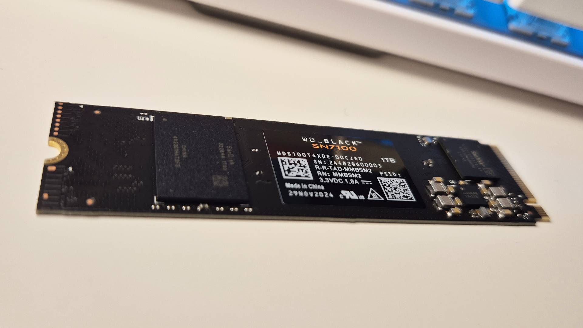 Photo of a black SSD sitting on a white gaming desk with a keyboard in the background.