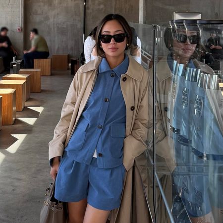 a woman wearing a trench coat, a blue top and matching shorts and a tan leather bag