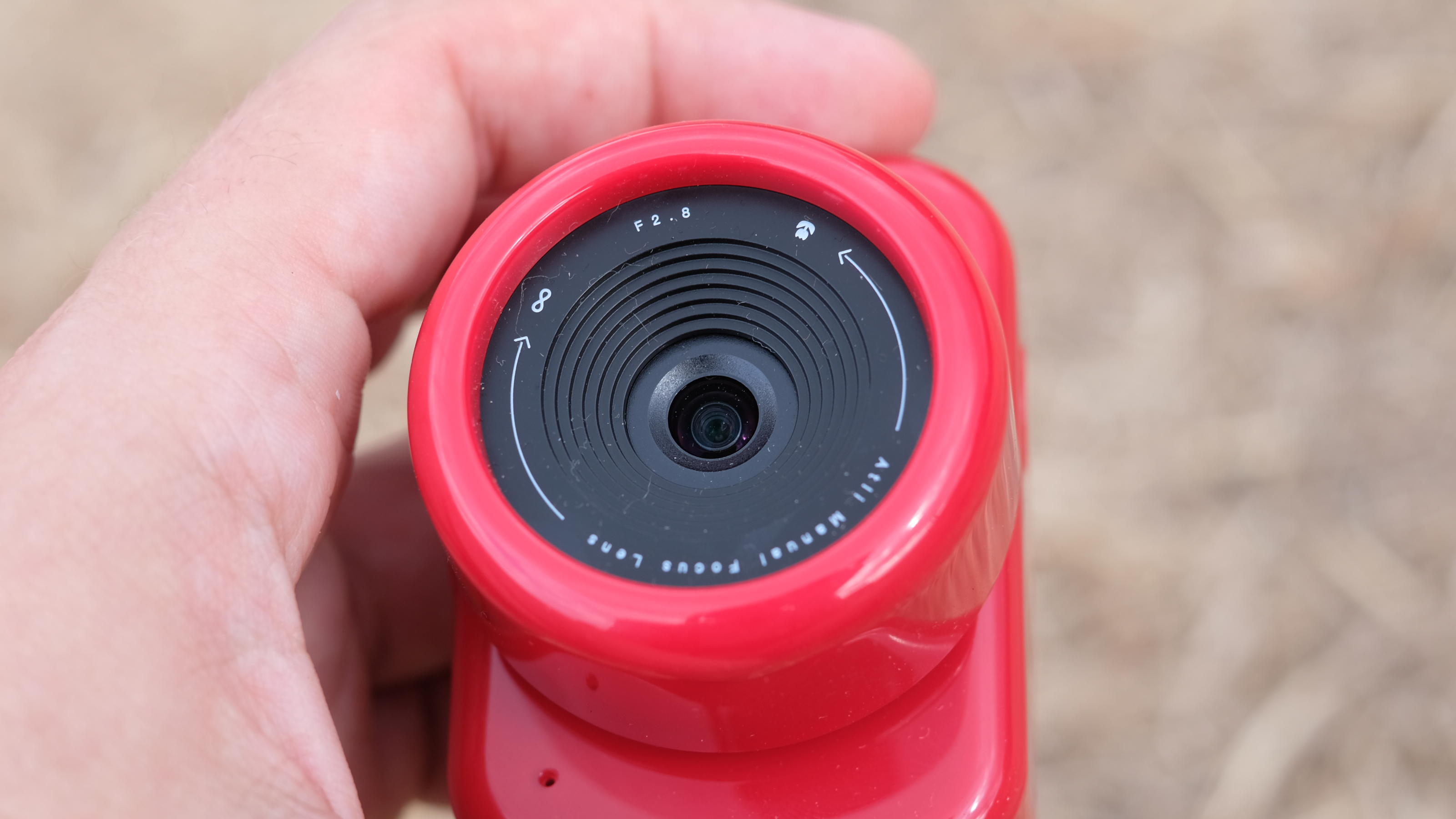 Photograph of the ATLi Eon time-lapse camera in red, close-up view of lens with focusing instructions visible