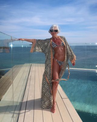 Woman wearing a kaftan and matching swimsuit on a wood deck near the ocean