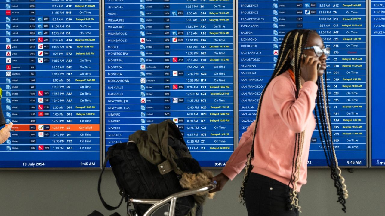 A woman walks past a board showing flight delays at Dulles International Airport on July 19, 2024.