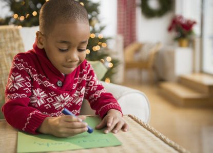 boy drawing on paper with Christmas jumper on as schools close early for Christmas