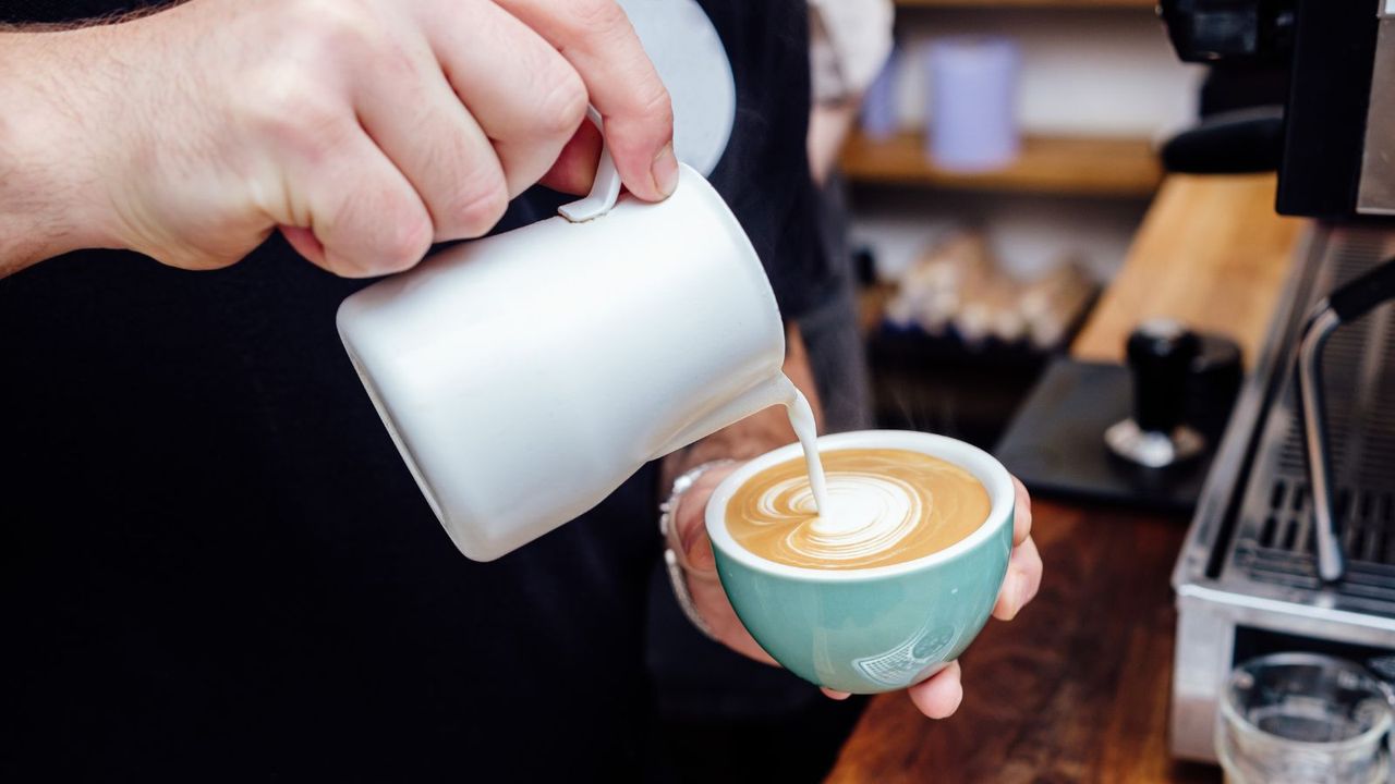 Textured milk in a jug bring poured into a cup to make latte art