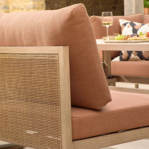 A close up of the back corner of Next's Abel Rattan Garden Modular Sofa and Table Lounge Set showing the rattan back of the sofa and rust brown cushion with a glass of wine and platter on the table