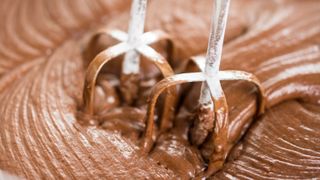a close up of the beaters on a hand mixer mixing a chocolate recipe