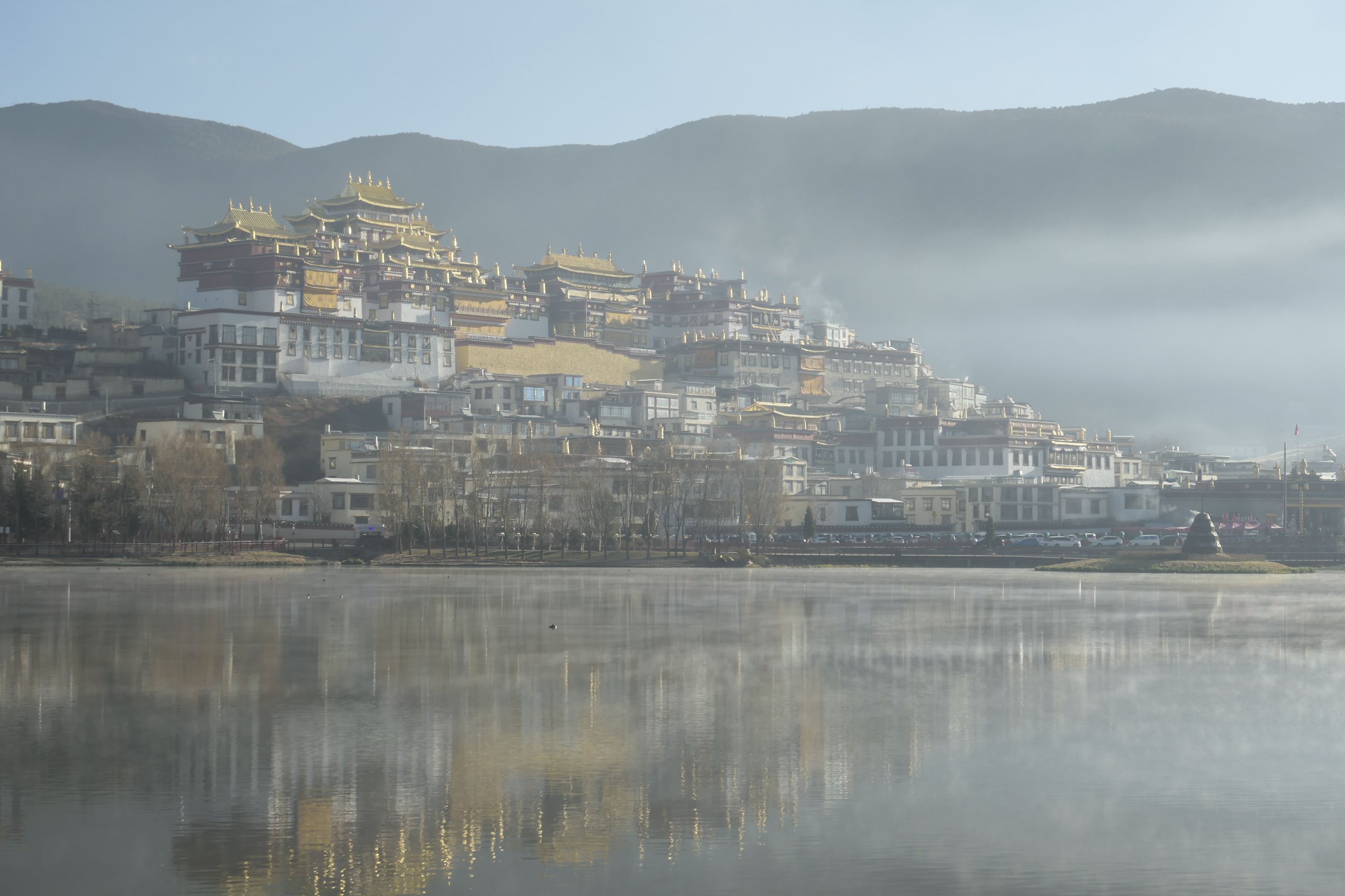 A buddhist monastery and town reflected in a still lake at first light, with a touch of mist