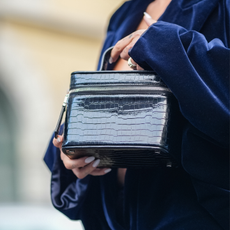 A woman in a chic navy velvet suit is seen holding a black croc vanity case that could be one of the best make-up bags