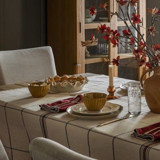 A cream and black checked table cloth on a wooden table, decorated with autumnal flowers and a pie dish