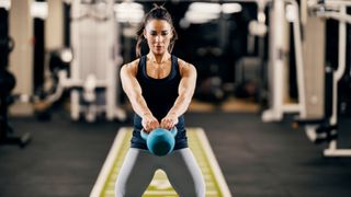 Woman holding a kettlebell in front of her with both hands as it swings in front of her body during ab exercise
