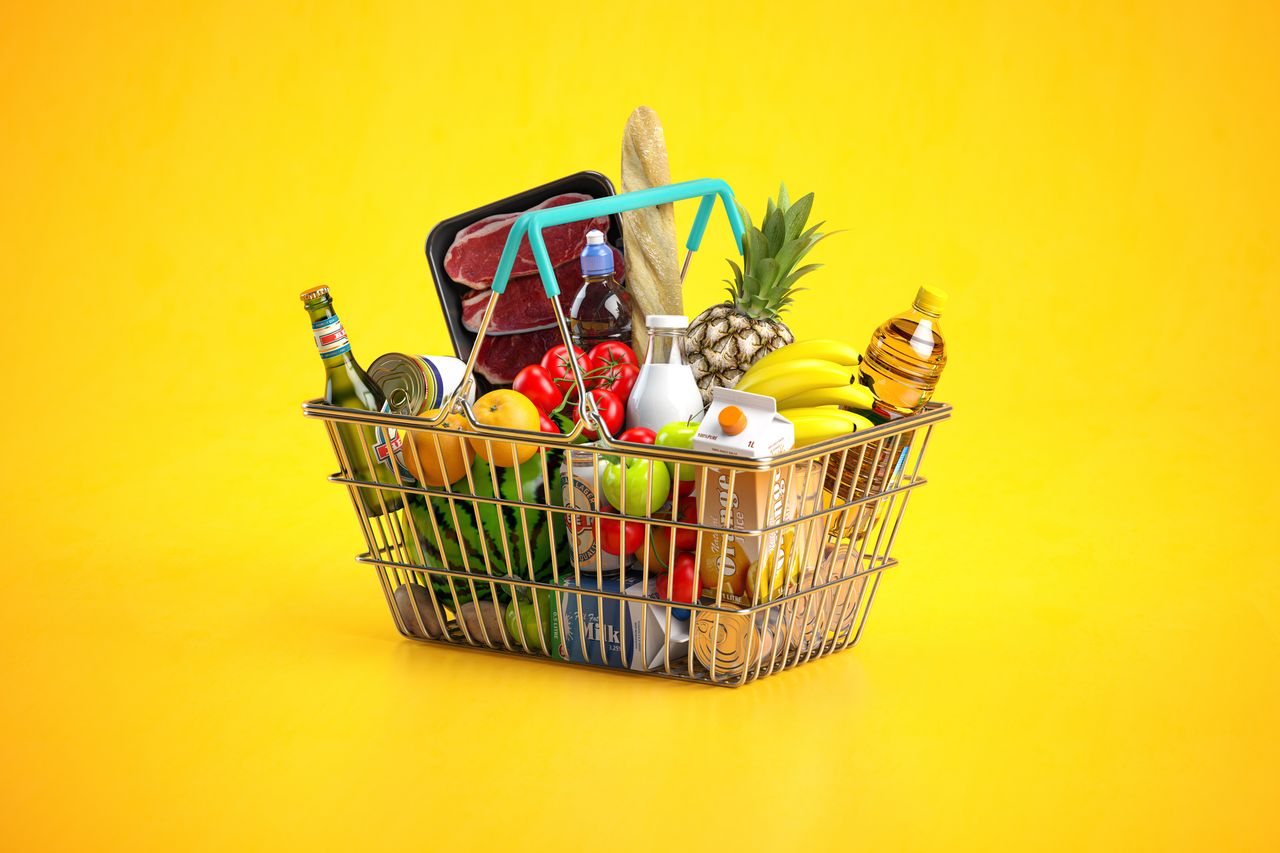 Shopping basket full of variety of grocery products, food and drink on yellow background