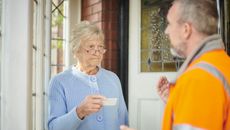 Senior woman holding business card and looking warily at tradesman. 