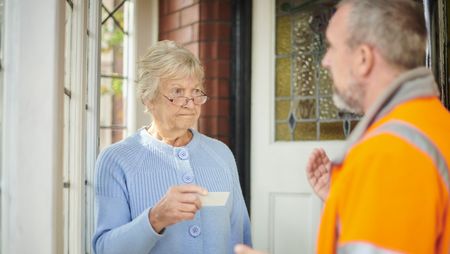 Senior woman holding business card and looking warily at tradesman. 