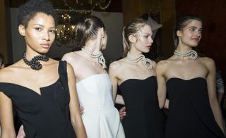 3 models wearing black evening gowns and 1 wearing white evening gown with pearl necklaces