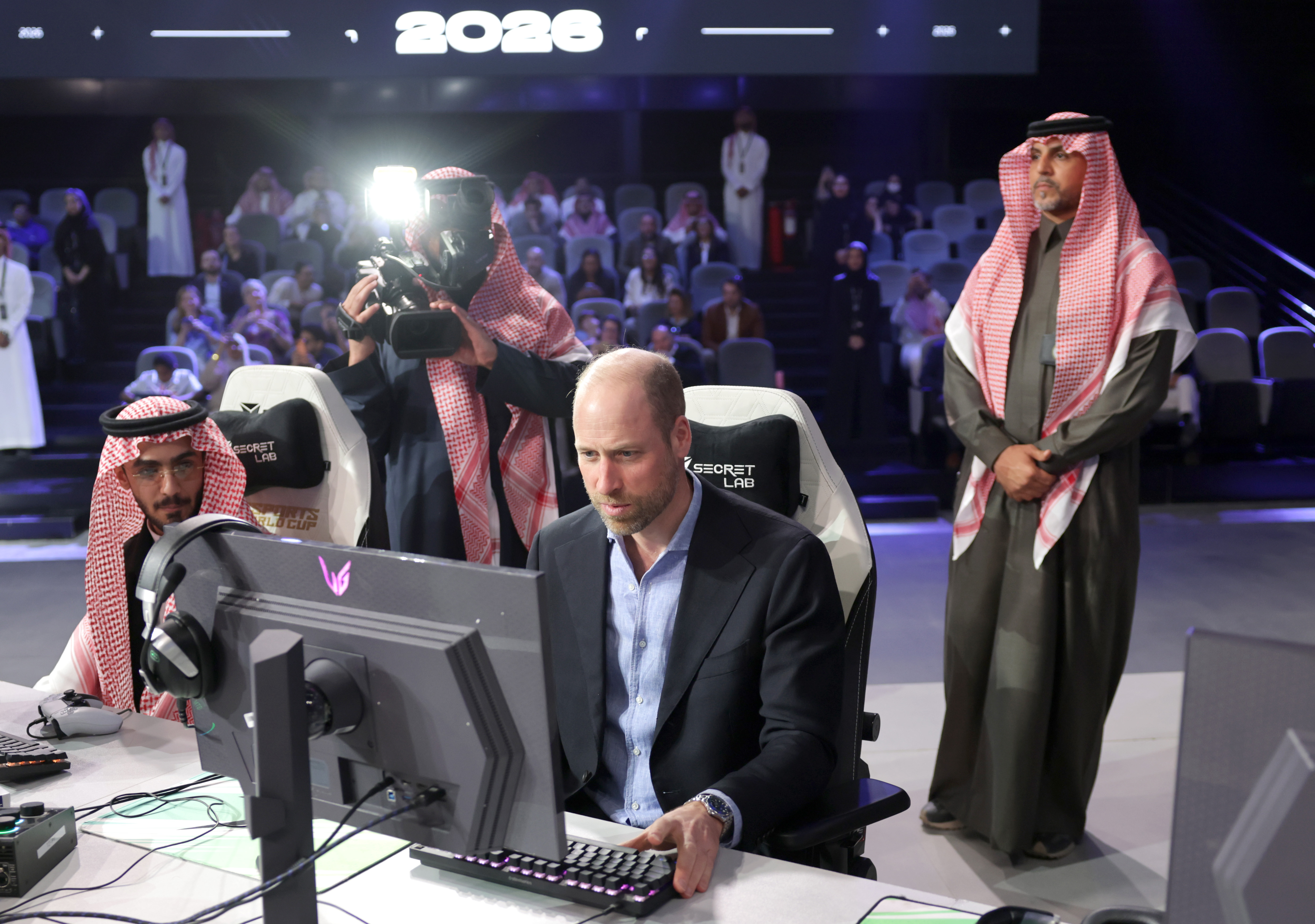 Prince william playing a game on a computer with Saudi men standing behind him