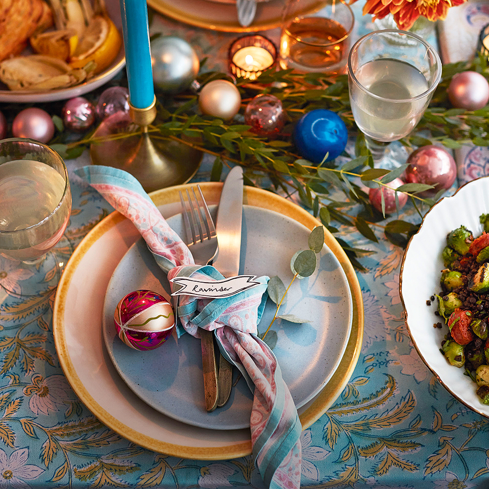 Christmas napkin tied around cutlery with colourful baubles, foliage and candles