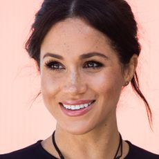 Meghan Markle wearing a black dress with her hair up in front of a plain backdrop