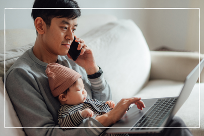 man holding baby while on phone and using computer