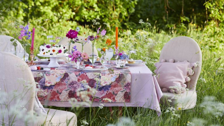 A pretty table setting in a garden tea party under the shade of a tree in summer with wildflowers and a floral tablecltoh
