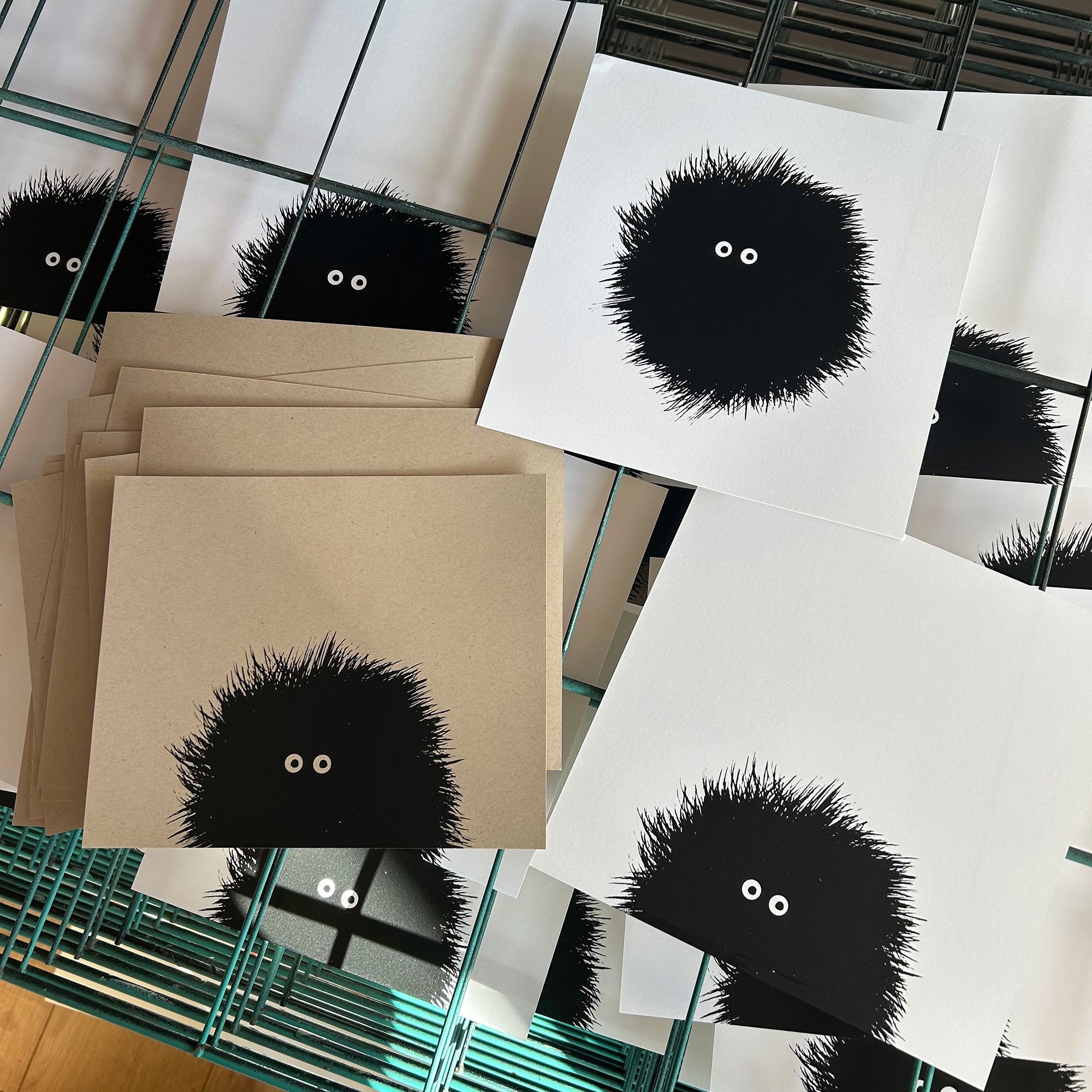 Array of screenprints of black hairy creature with large eyes resting on drying racks