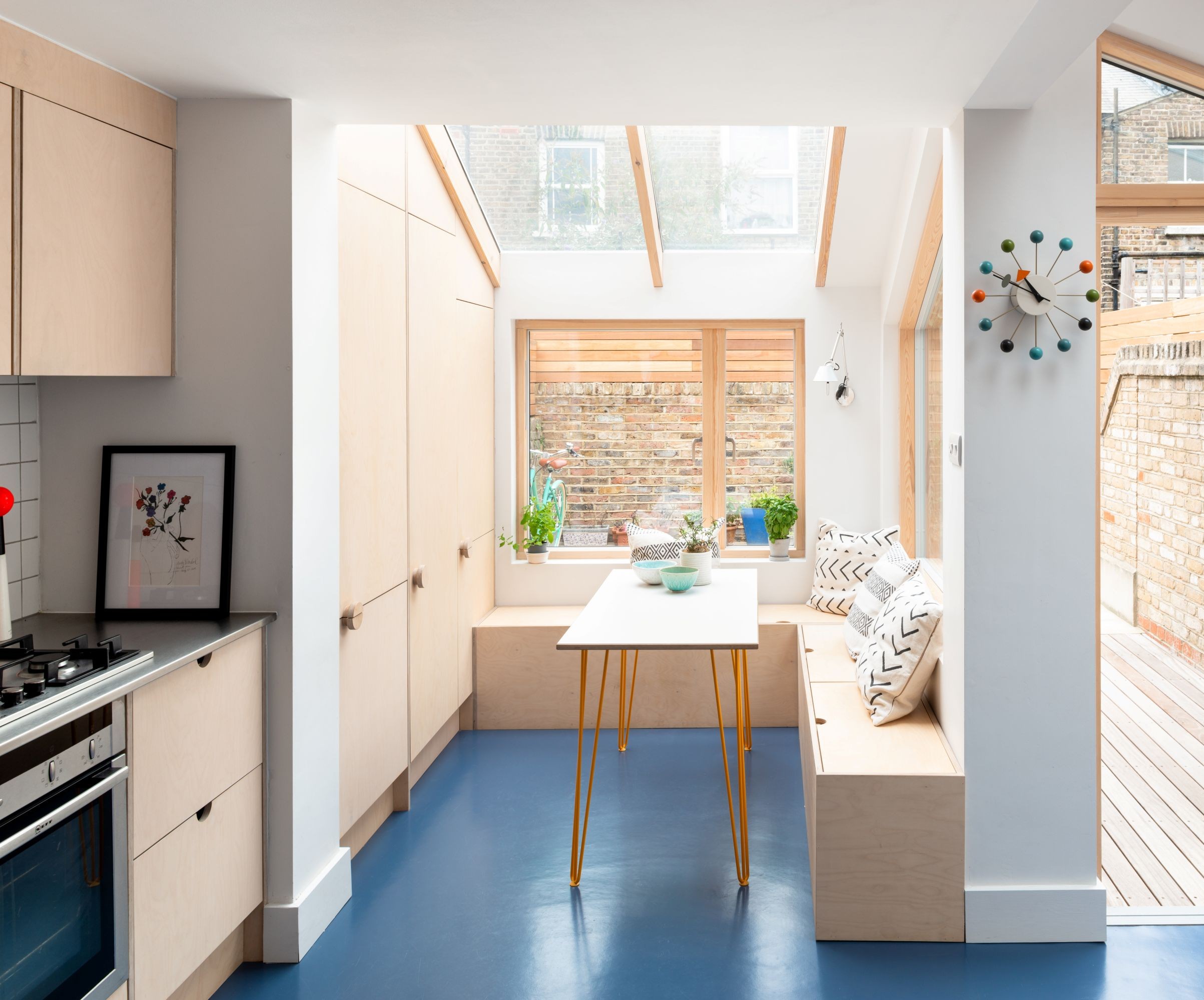 A plywood kitchen with small dining table and built in bench seating in a small extension with a glass roof