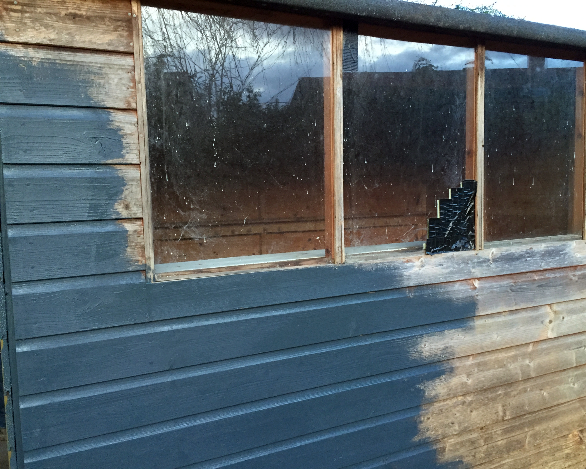 old wooden shed half painted a dark gray tone