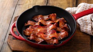 A red cast iron skillet with cooked bacon