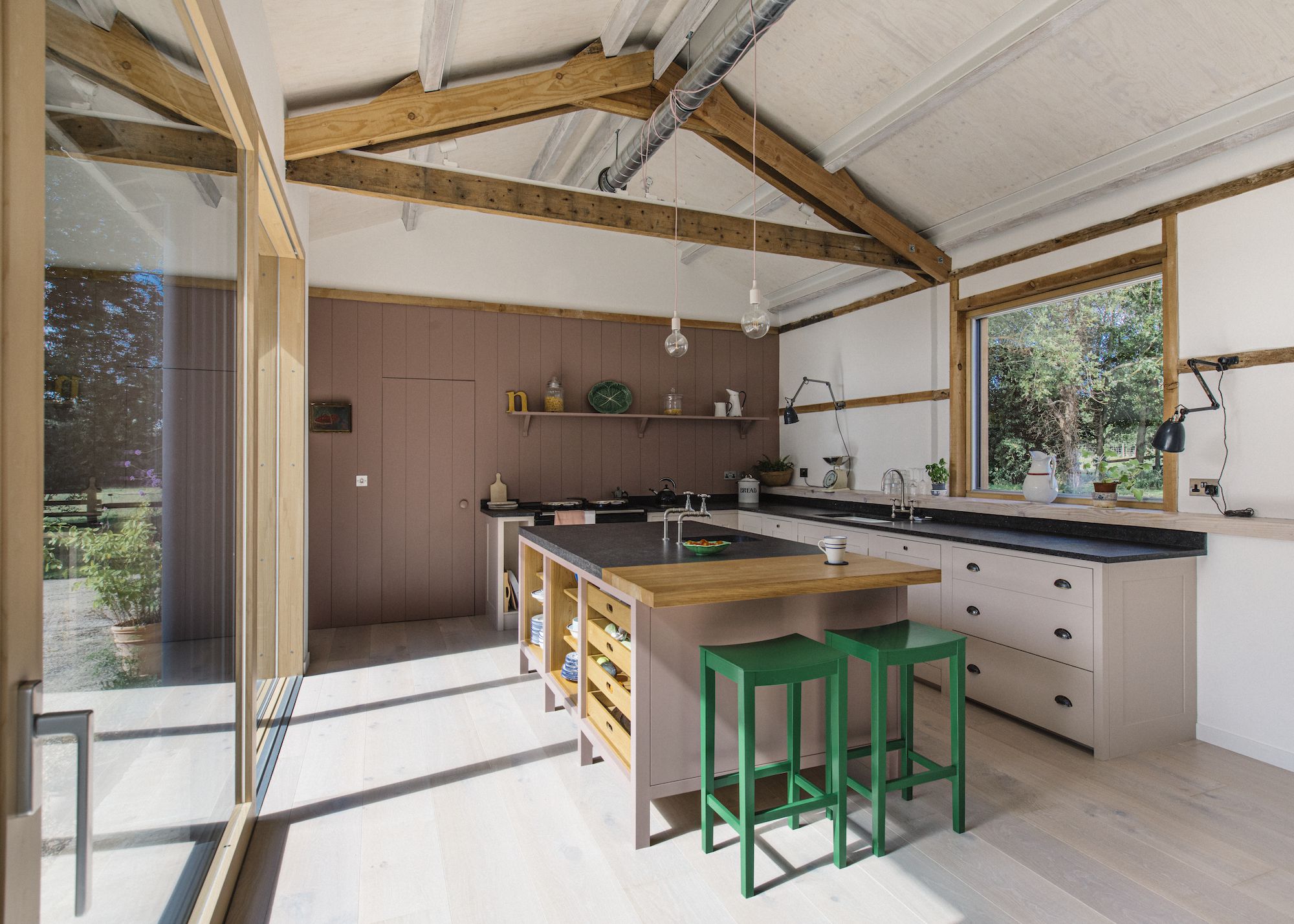 A farmhouse kitchen with an wooden island. Beside the island are two green bar stools.